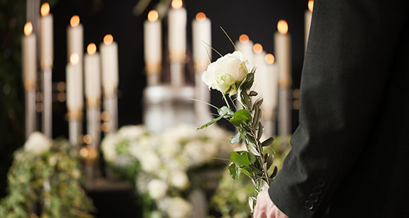a mourner at a funeral holding a white rose in front of a memorial alter with flowers and candles