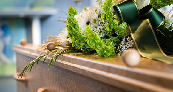a casket with an arrangements of flowers with a green ribbon on top